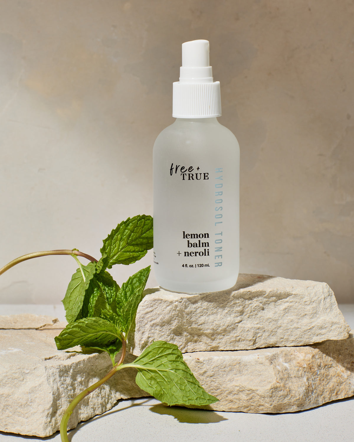 Lemon Balm + Neroli hydrosol toner on stone with botanicals