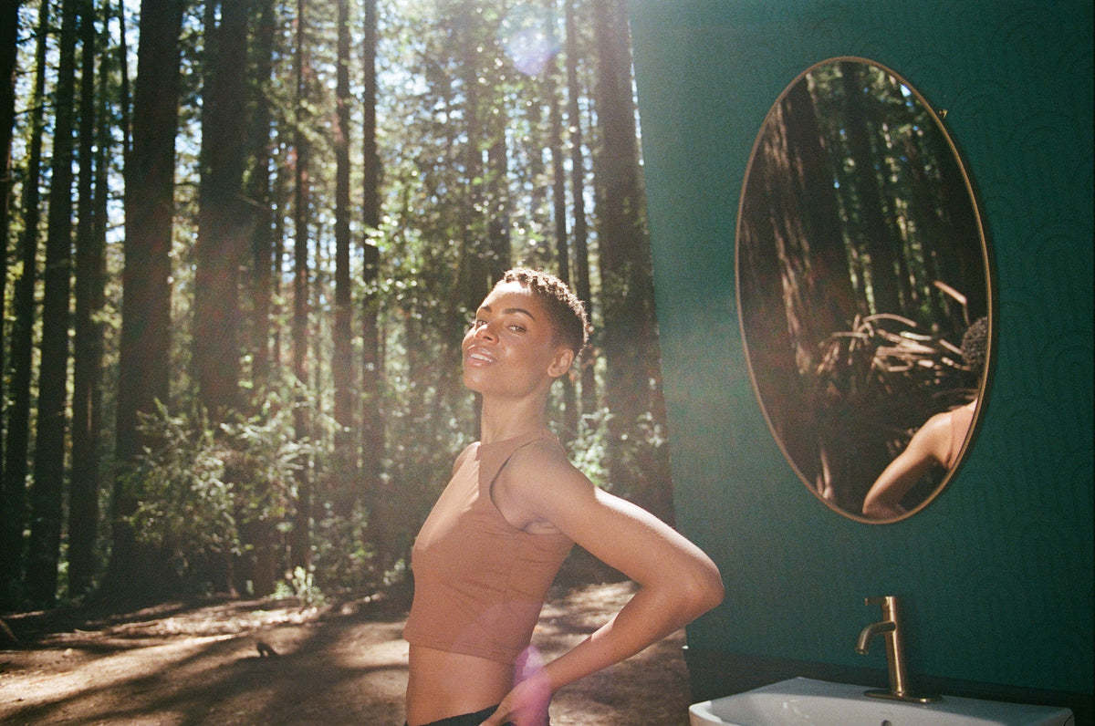 Forest vanity — smiling woman beside a mirror in the redwoods