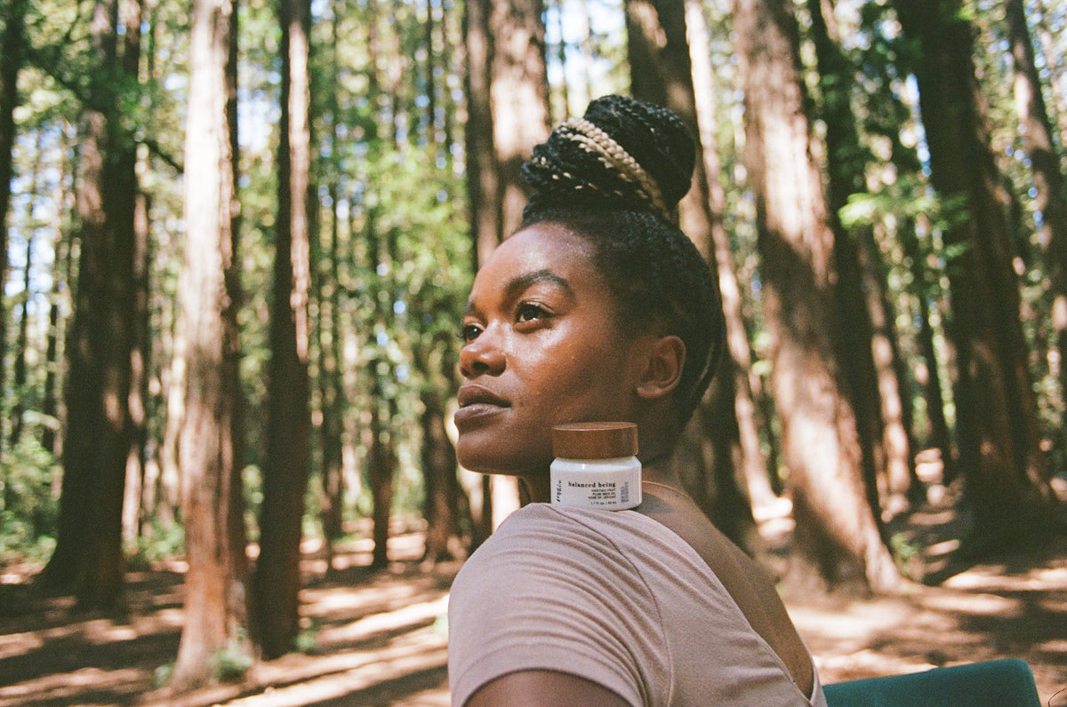 Woman in sunlit redwoods with Balanced Being resting on her shoulder