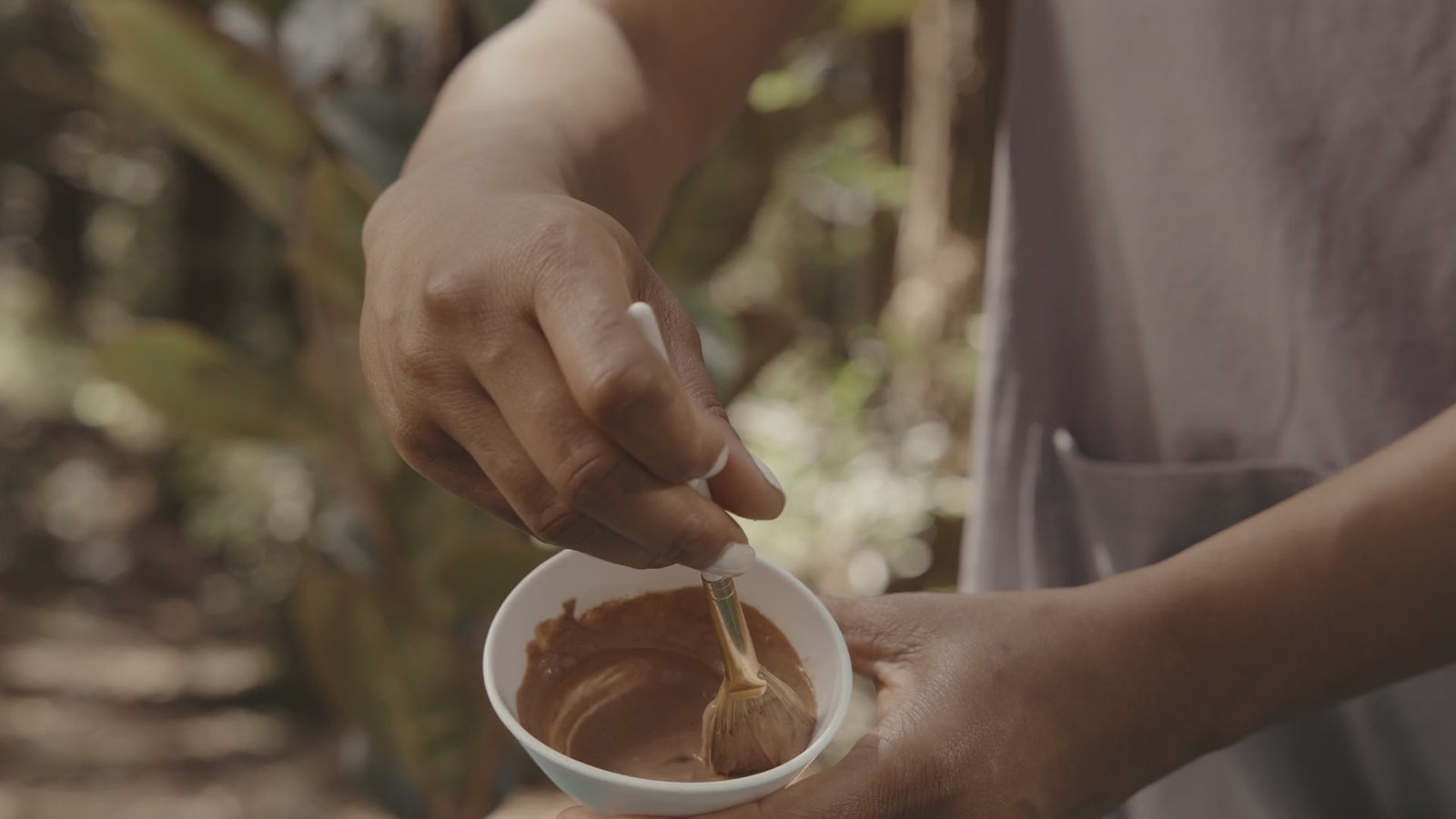 A professional blends a warm terracotta-colored mask with a fan brush.